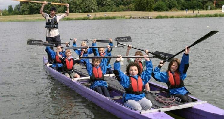 bellboat helm - A group of children in a bellboat waving their paddles and cheering