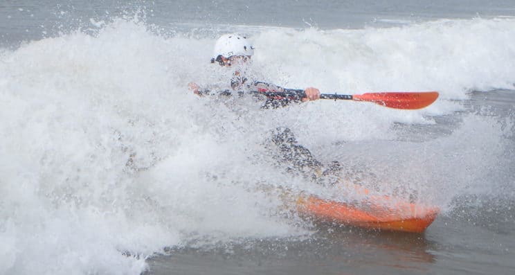 Advanced Surf Kayak Leader. A surf kayaker rides a large breaking wave.