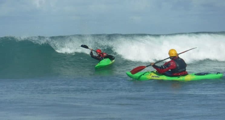 Surf Kayak Leader. A paddler playing on a wave whilst a leader observes.
