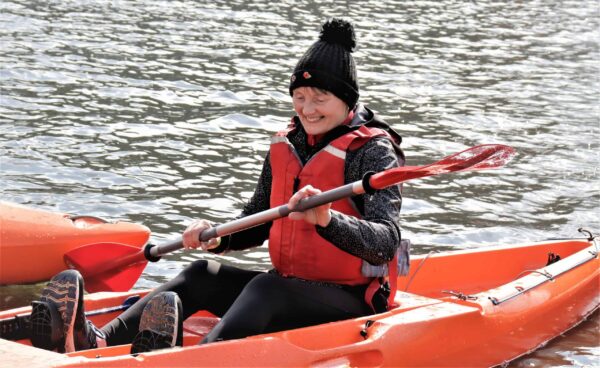 Female paddler sits in a canoe wearing a life jacket. British Canoeing Paddle Safer Provider eLearning